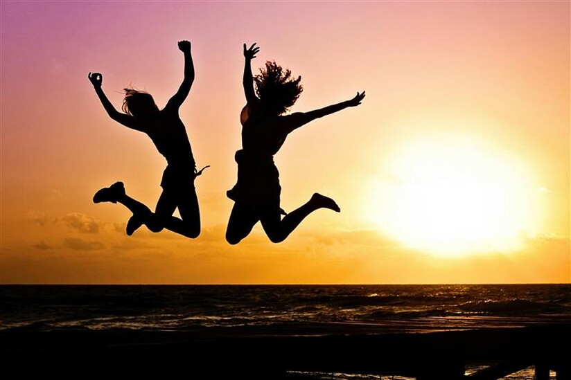 Two youth jumping with their arms in the air in front of a sunset