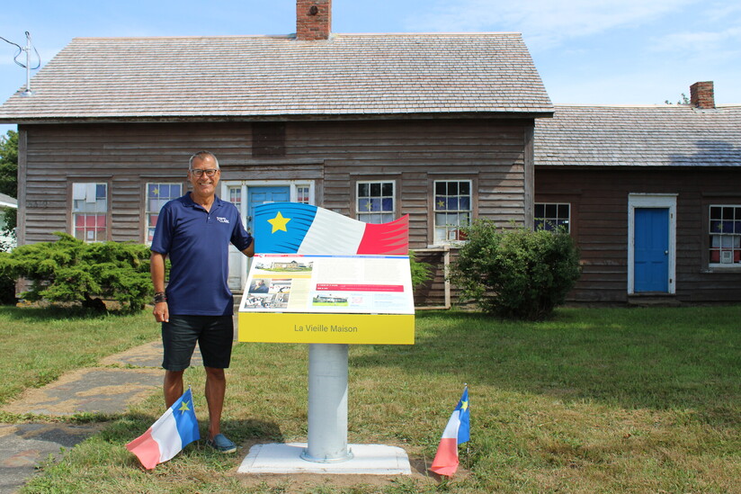 An image of Councillor Carl Deveau in front of a new interpretive pannel at La Vieille Maison in Meteghan.